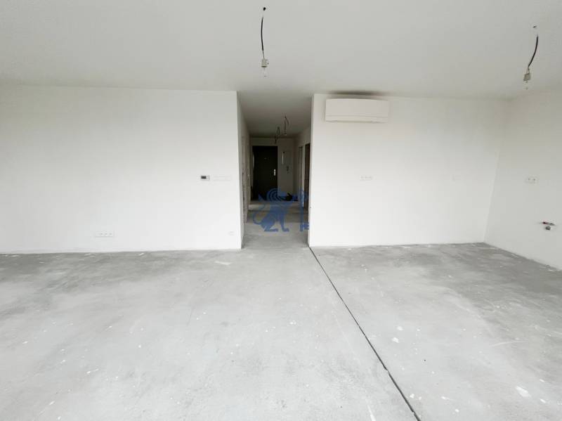 Prázdný pokoj ve 3-pokojovém bytě s betonovou podlahou a bílými stěnami.