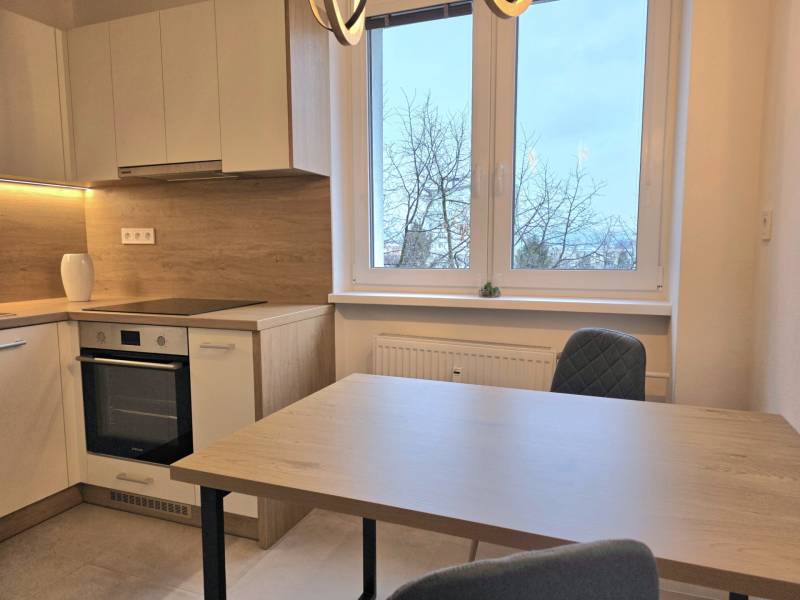 Kuchyně s kuchyňskou linkou, jídelním stolem a židlemi, ve 3-pokojovém bytě s podlahou s dřevěným dekorem.