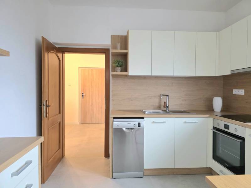 Světlá kuchyně s vestavěnými spotřebiči a podlahou s dřevěným dekorem v 3-pokojovém bytě.