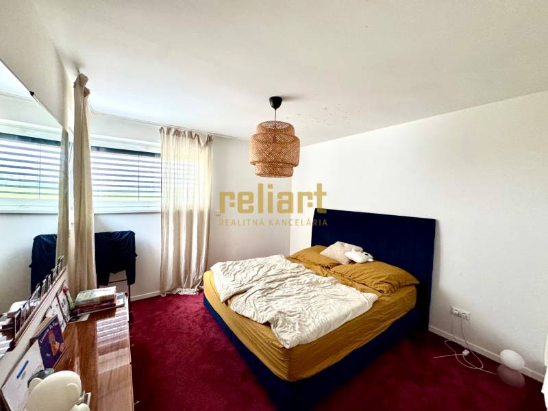 Ložnice v rodinném domě s červeným kobercem, modrou postelí a velkým oknem.