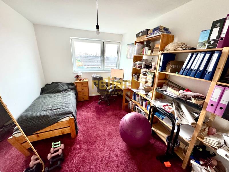 Pokoj v rodinném domě se stolem, postelí, policemi a červeným kobercem.