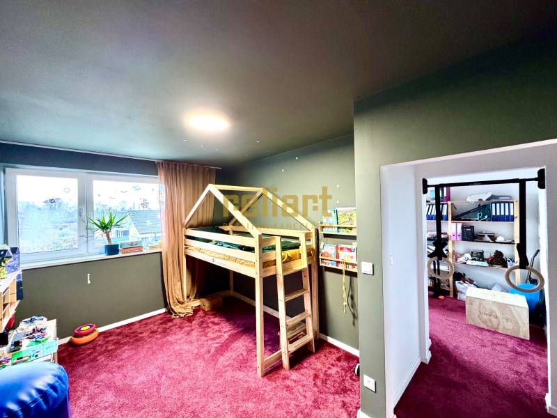 Dětský pokoj v rodinném domě s dřevěnou postelí a bordovým kobercem.