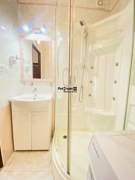 Koupelna s rohovou sprchou, umyvadlem a pračkou v 2-pokojovém bytě.