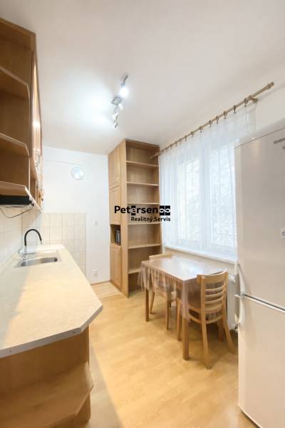 Kuchyně v 2-pokojovém bytě s podlahou s dřevěným dekorem, jednoduchý nábytek a spotřebiče.