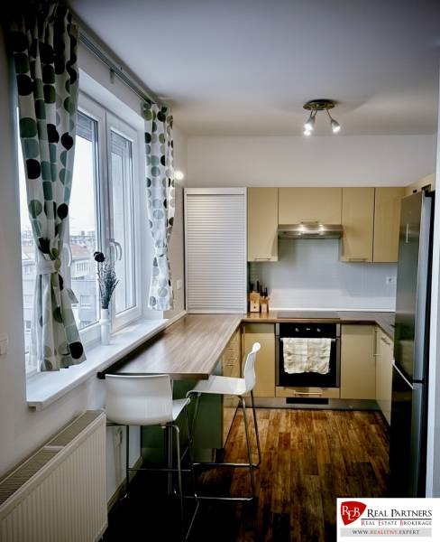 Kuchyně v 3-pokojovém bytě s barovým pultem, podlahou s dřevěným dekorem a velkým oknem.