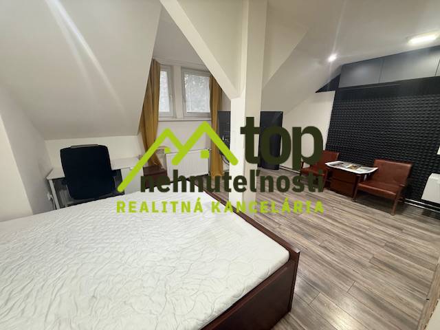 Ložnice v jednopokojovém bytě s podlahou s dřevěným dekorem a pracovním stolem.