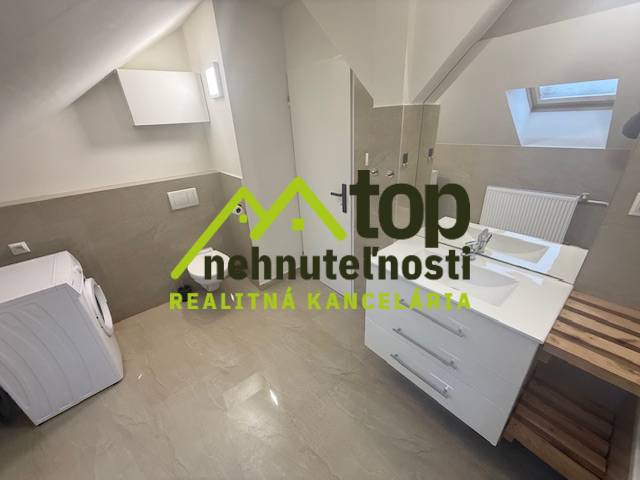 Koupelna v podkroví 1-pokojového bytu s pračkou a umyvadlem, podlaha s dřevěným dekorem.