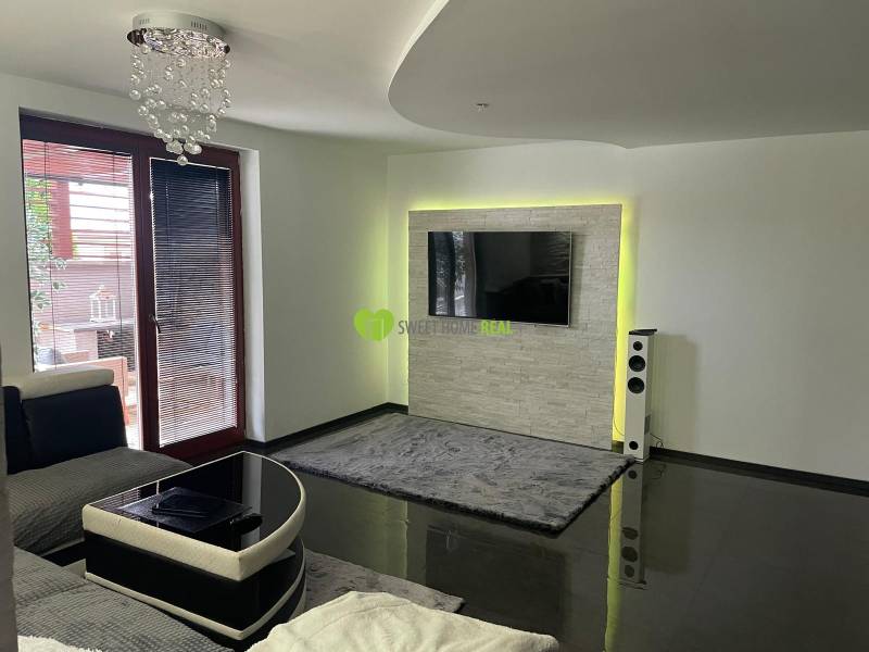 Obývací pokoj v rodinném domě s lesklou podlahou a TV na stěně.