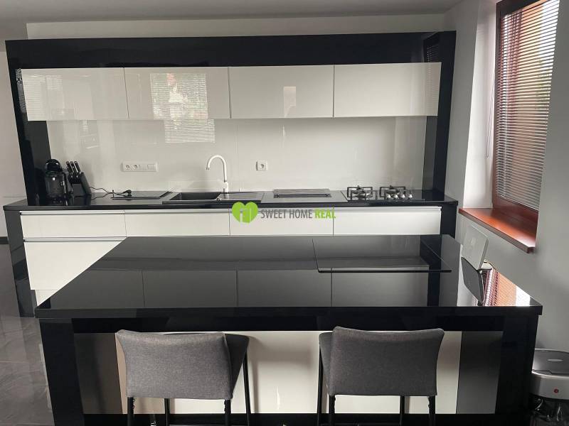 Kuchyně v rodinném domě s lesklým černo-bílým nábytkem a jídelním pultem.