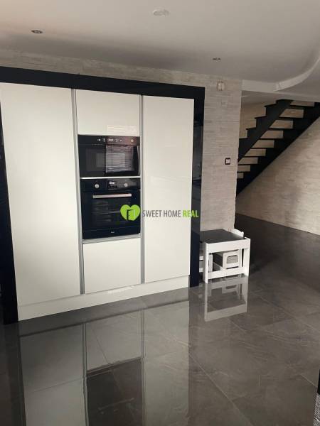 Kuchyně v rodinném domě s lesklou černou podlahou a bílými spotřebiči.