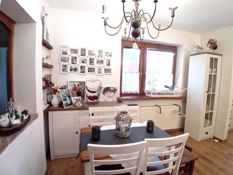 Jídelna v rodinném domě s bílým nábytkem, obrázky na stěně a ozdobným lustrem.