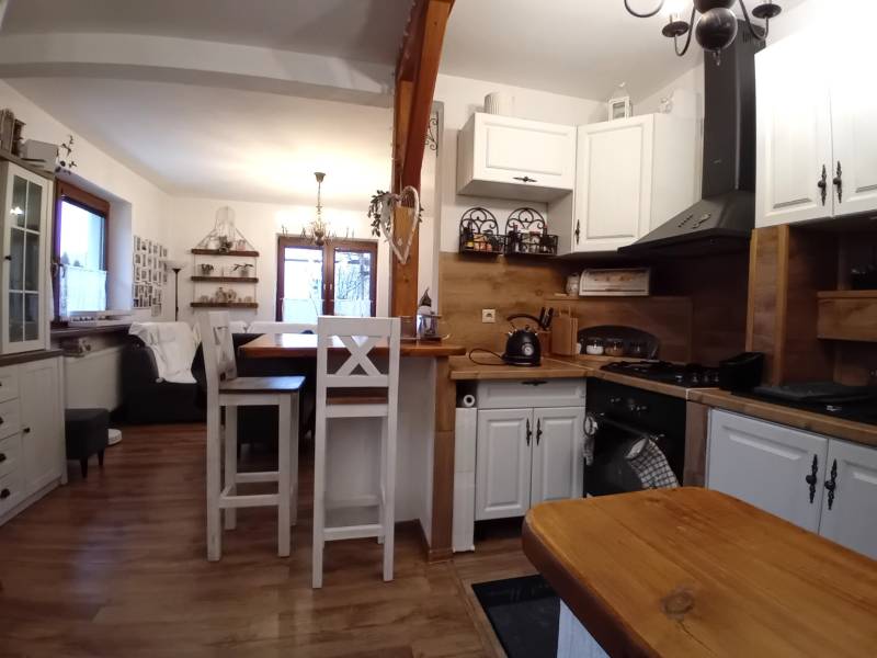 Kuchyně a obývací pokoj v rodinném domě s podlahou s dřevěným dekorem a bílým nábytkem.