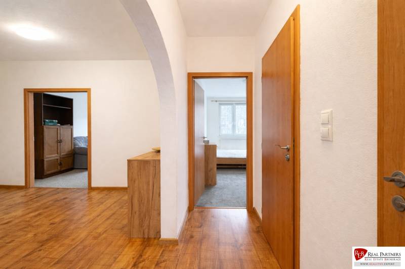 Chodba s podlahou s dřevěným dekorem, dveře vedou do pokojů ve 4pokojovém bytě.