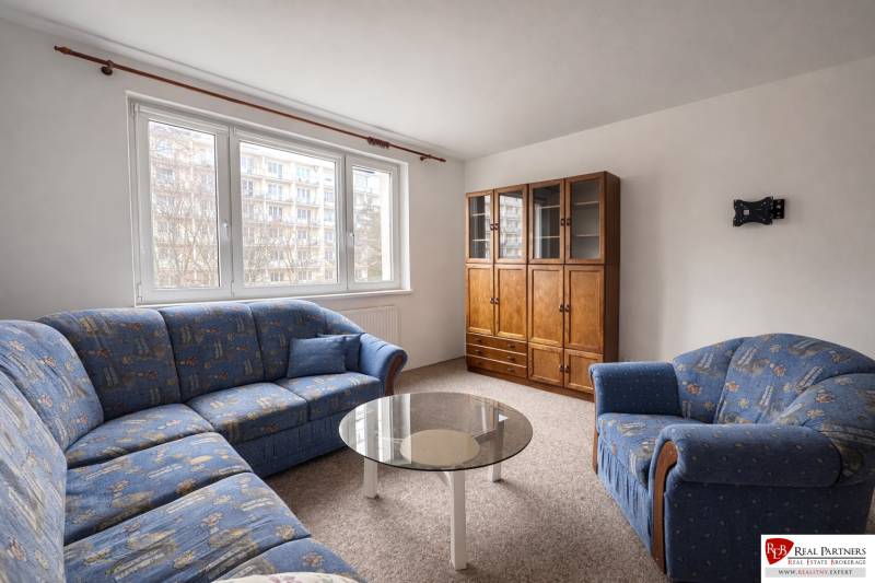 Obývací pokoj ve 4-pokojovém bytě s modrou sedací soupravou a dřevěným nábytkem.