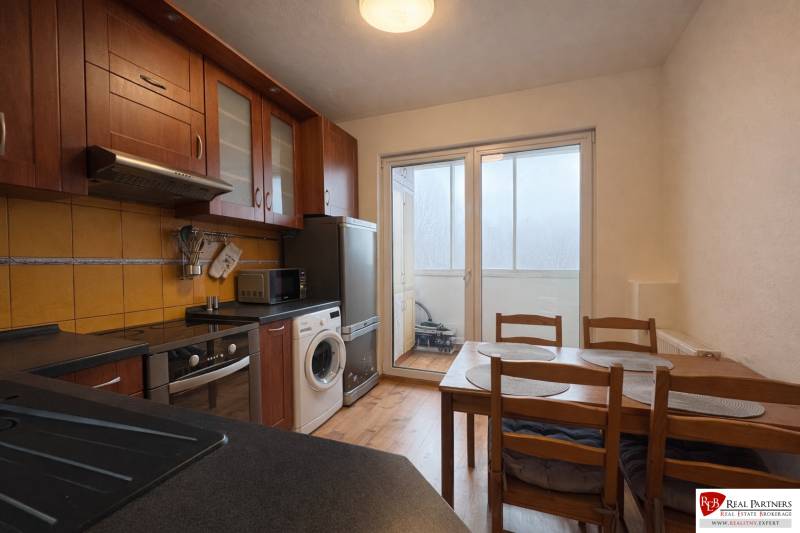 Kuchyně ve 4-pokojovém bytě s tmavým nábytkem a podlahou s dřevěným dekorem.