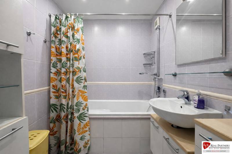 Koupelna se závěsem s listovým motivem ve 4-pokojovém bytě s vanou a umyvadlem.