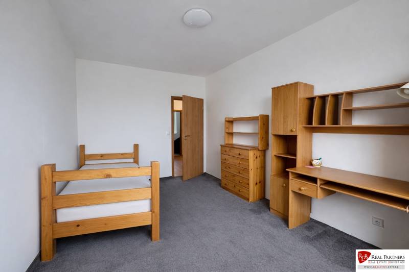 Pokoj ve 4pokojovém bytě se světlým nábytkem a šedým kobercem.