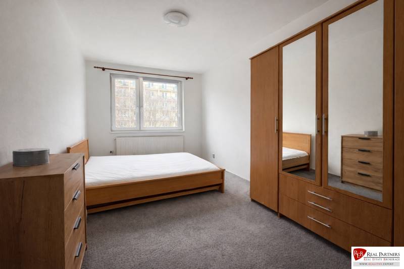 Ložnice ve čtyřpokojovém bytě s dřevěným nábytkem a kobercem.