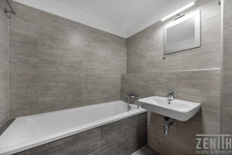 Koupelna v 2-pokojovém bytě s vanou, umyvadlem a šedými obklady.