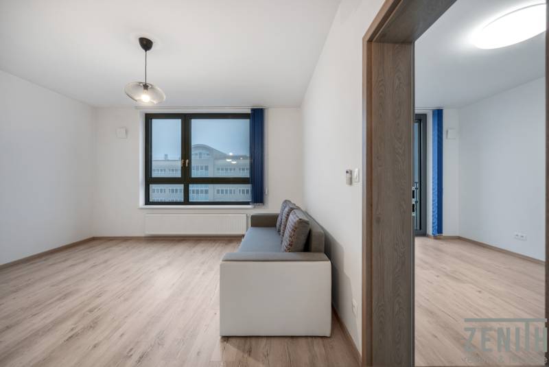 Obývací pokoj s pohovkou, velkým oknem a podlahou s dřevěným dekorem ve 2pokojovém bytě.