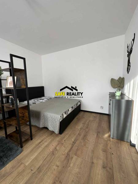 Ložnice v jednopokojovém bytě s podlahou s dřevěným dekorem a minimalistickým zařízením.