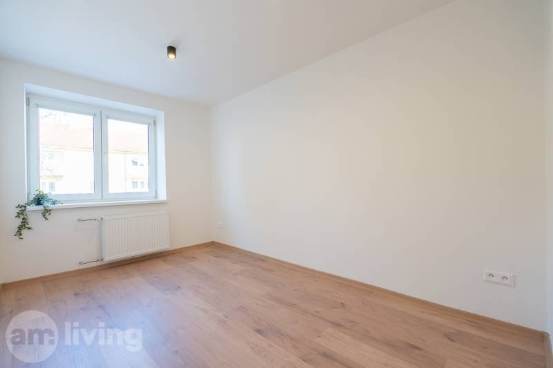 Světlý pokoj s podlahou s dřevěným dekorem v 3-pokojovém bytě se světlem nad oknem.