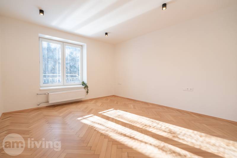 Světlý pokoj ve 3-pokojovém bytě s podlahou s dřevěným dekorem a velkým oknem.