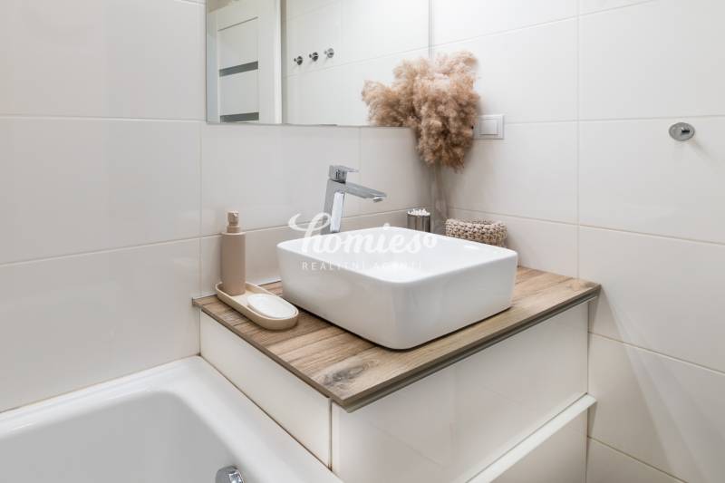 Koupelna v 2-pokojovém bytě s umyvadlem, podlahou s dřevěným dekorem a dekorativním rostlinným aranžmá.