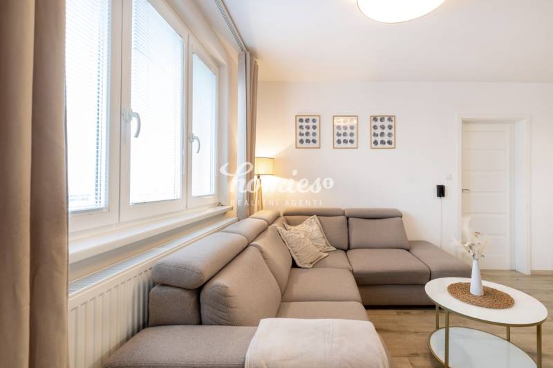 Obývací pokoj v 2-pokojovém bytě s pohodlnou sedačkou a dekoracemi na stěně.