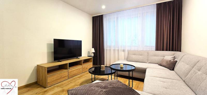 Obývací pokoj v 3-pokojovém bytě s pohovkou, televizí a stolkem na podlaze s dřevěným dekorem.