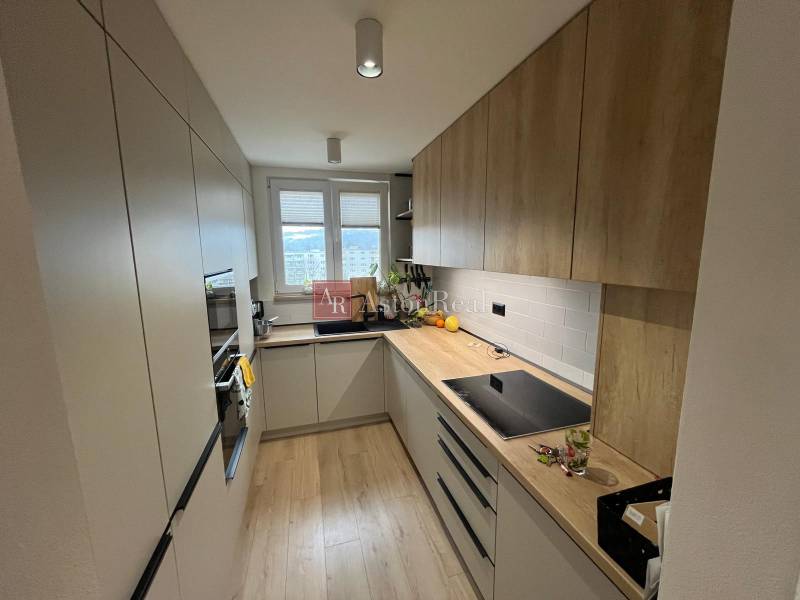 Kuchyně ve 4-pokojovém bytě s linkou, spotřebiči a podlahou s dřevěným dekorem.