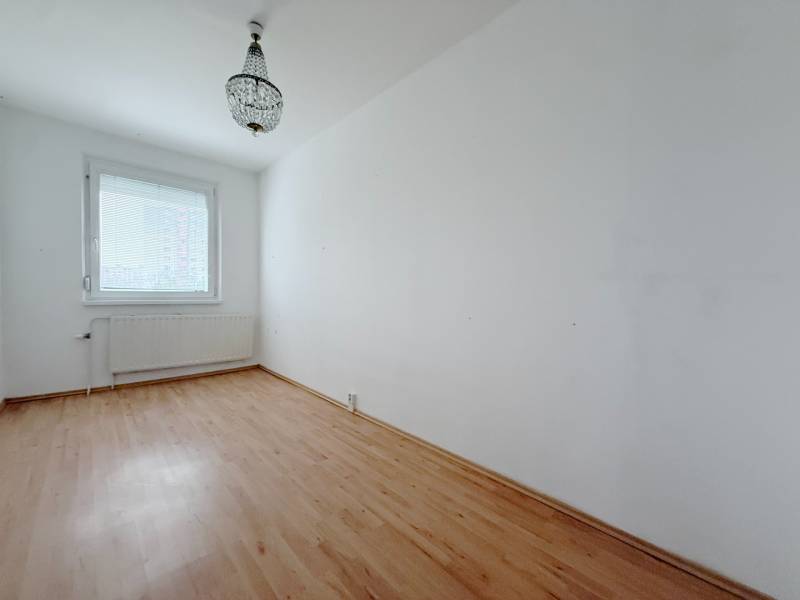 Pokoj ve čtyřpokojovém bytě s lustrem a podlahou s dřevěným dekorem.