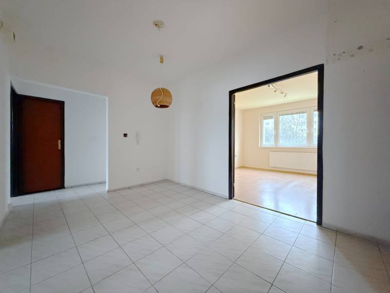 Chodba s dlažbou vede do světlého obývacího pokoje se vstupem na podlahu s dřevěným dekorem.