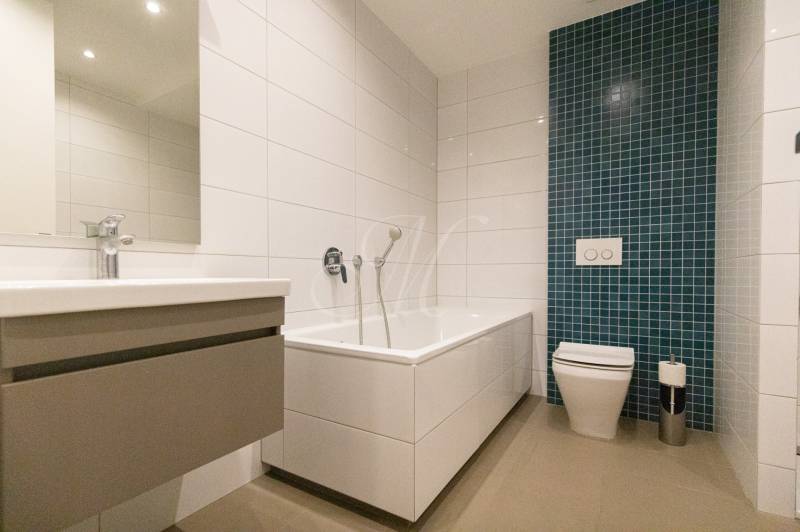 Koupelna v 2-pokojovém bytě s vanou, umyvadlem a zeleným obkladačkovým panelem.