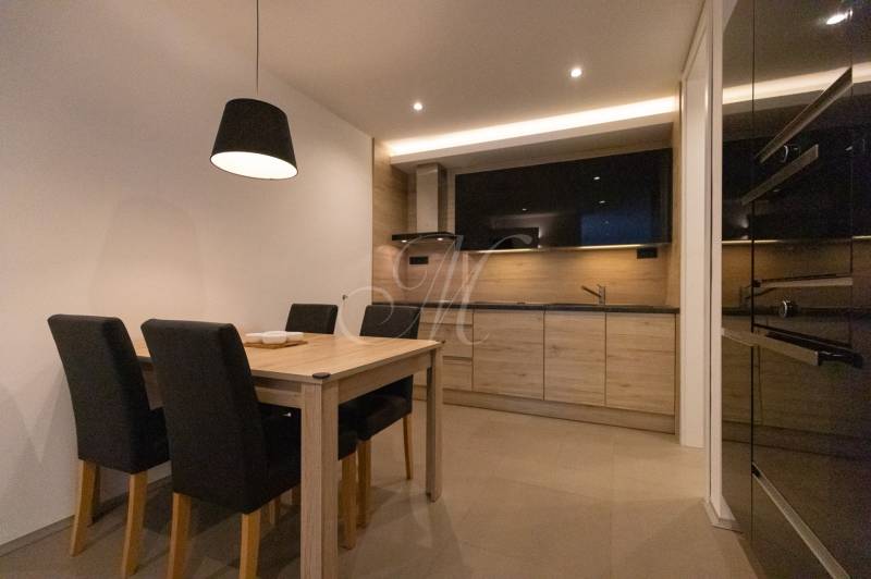 Kuchyně v 2pokojovém bytě s dřevěným dekorem, jídelním stolem a černými židlemi.