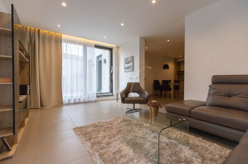 Obývací pokoj v 2-pokojovém bytě s pohodlnou sedačkou, křeslem a skleněným stolkem.