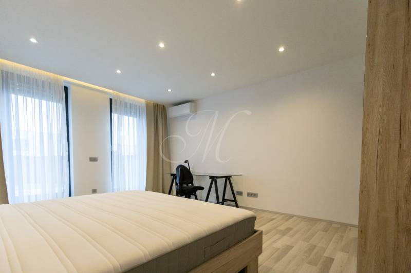 Ložnice v dvoupokojovém bytě s postelí, stolem a podlahou s dřevěným dekorem.