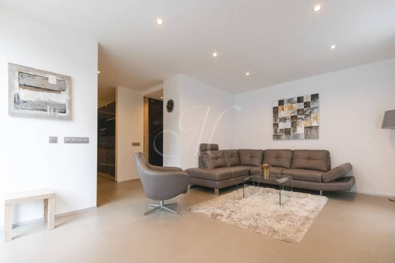 Obývací pokoj v 2pokojovém bytě s pohovkou, křeslem, kobercem a obrazy na stěně.