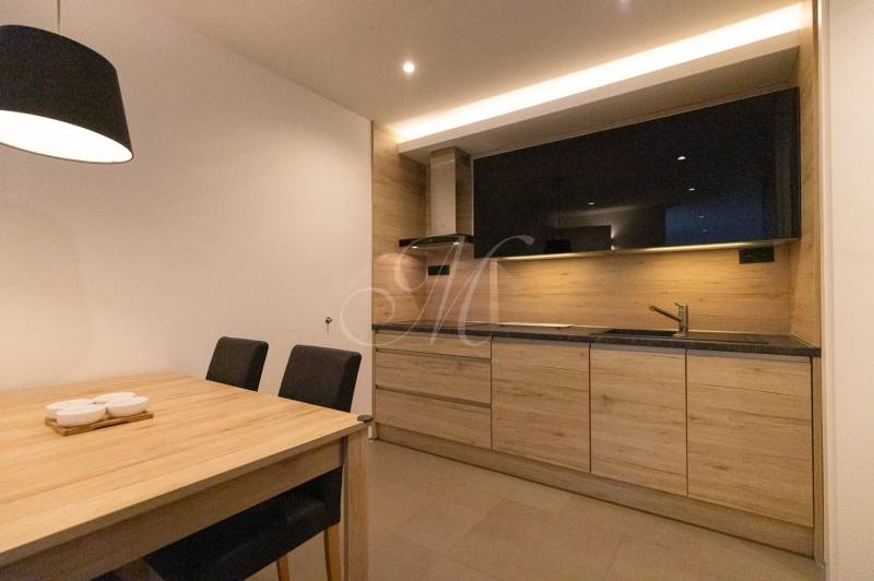 Kuchyně 2pokojového bytu s minimalistickým designem, dřevěným dekorem a jídelním stolem.