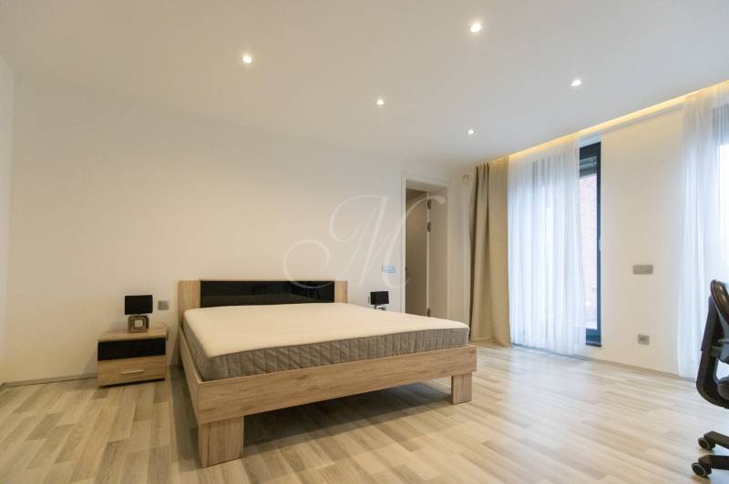 Ložnice v 2pokojovém bytě s postelí, nočním stolkem a podlahou s dřevěným dekorem.