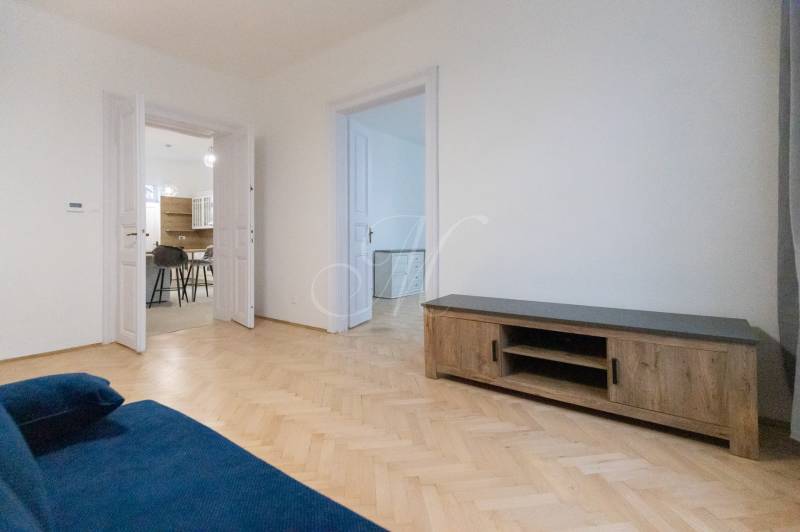 Obývací pokoj 3pokojového bytu s modrou sedačkou a podlahou s dřevěným dekorem.