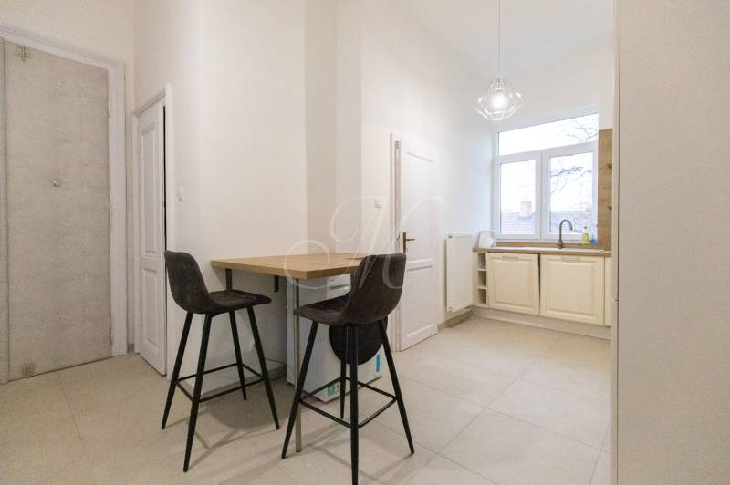 Kuchyně ve 3-pokojovém bytě s barovým pultem, dvěma židlemi a velkým oknem.