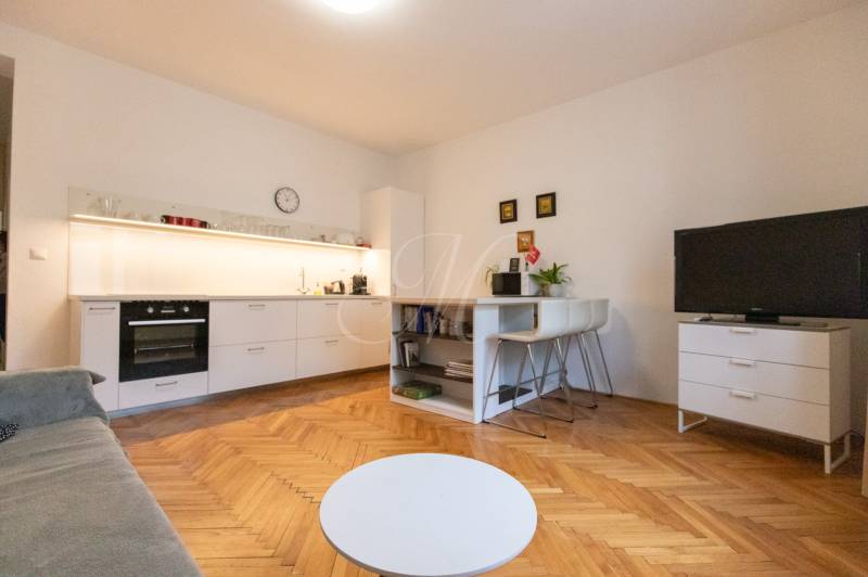 Obývací pokoj v 2pokojovém bytě s kuchyní, podlaha s dřevěným dekorem, TV a stolek.