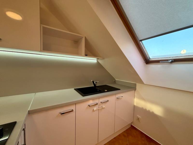 Kuchyňská linka v 2pokojovém bytě s bílými skříňkami a velkým střešním oknem.