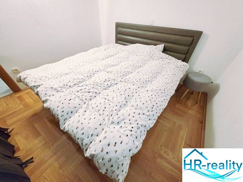 Rekreační apartmán s postelí, dřevěným dekorem podlahy a malým nočním stolkem.