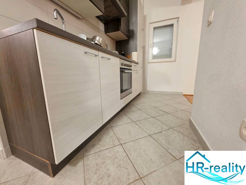 Kuchyně v rekreačním apartmánu s dlažbou a moderní linkou s tmavými skříňkami.