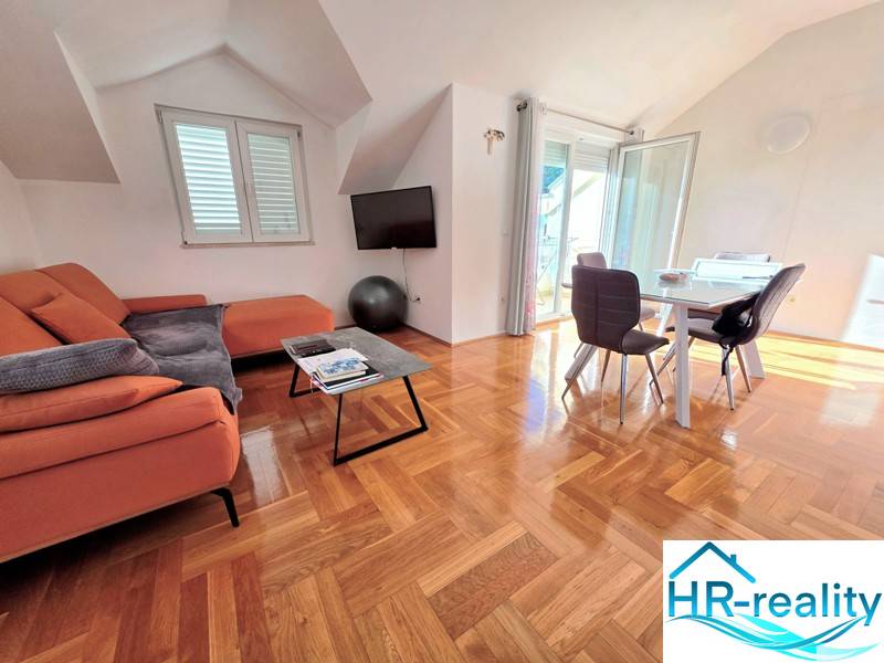 Rekreační apartmán s oranžovou pohovkou, jídelním stolem a podlahou s dřevěným dekorem.