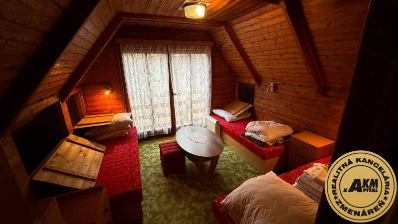 Interiér chaty s dřevěným obložením, třemi postelemi a kulatým stolkem.