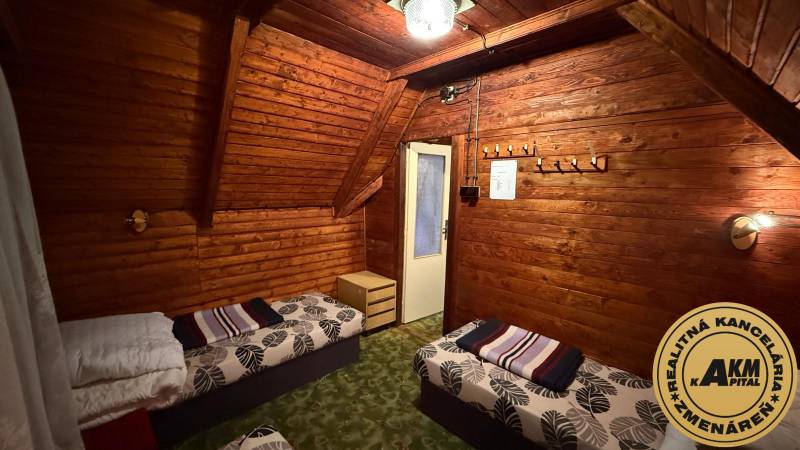 Interiér chaty s dřevěným obložením, postelemi a lustrem, útulné prostředí pro relaxaci.