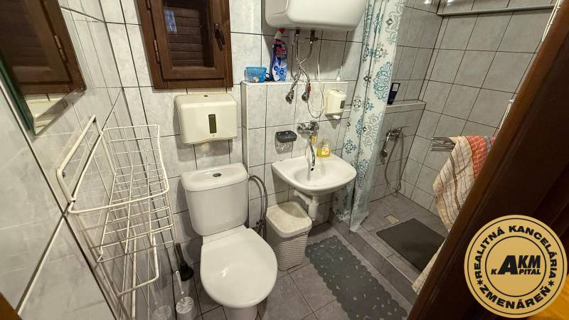 Koupelna v chatě se sprchou, umyvadlem, toaletou a obkladem na stěnách.